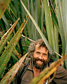 Trapper Bruce Reay amidst flax plants at Westland National Park. west coast, South Island, New Zealand