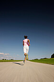 Woman jogging along road, Munsing, Bavaria, Germany