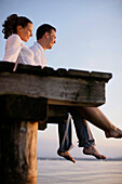 Couple sitting on a jetty, Ambach, Lake Starnberg, Bavaria, Germany