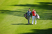 Zwei Golfspieler laufen über Golfplatz, Straßlach-Dingharting, Bayern, Deutschland