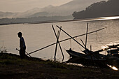 Silhouette of a boy with a watering can at the bank of the river Mekong, Luang Prabang, Laos
