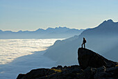 hiker on crag above fog bank in valley Gschnitztal, Bremer Huette, Stubaier Alpen range, Stubai, Tyrol, Austria