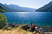 People sitting at the shore of Lake Crescent in the sunlight, Olympic Nationalpark, Washington, USA