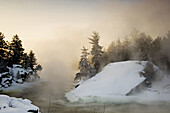 Tree silhouettes and rising mists near rapids of Wahnapitei River at sunrise. Ontario, Canada