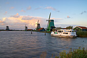 Ein Boot und Windmühlen am Abend, Freilichtmuseum Zaanseschans am Fluss Zaan, Holland, Europa