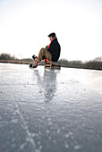 Senior man putting on ice skate, Lake Ammersee, Upper Bavaria, Germany