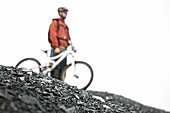 Mountainbiker standing on a scree looking at the view, Ischgl, Tyrol, Austria
