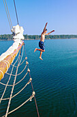Boy jumping off the bow of the Schooner Nathaniel Bowditch into the cold waters of Holbrook Bay (part of Penobscot Bay), Maine USA