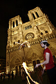 The night view of a street performer juggling flames in front of Notre-Dame Cathedral. Paris. France