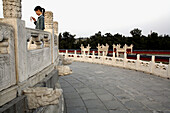 A young girl with her cellphone behind stone carved railings of Round Altar in Temple of Haven. Beijing. China