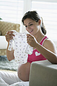 Schwangere Frau betrachtet Babykleidung
