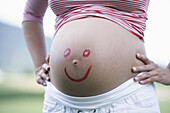 Pregnant woman with smiley face on belly, Styria, Austria