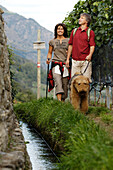 Ein Paar mit Hund wandert an einem Bach entlang, Vinschgau, Südtirol, Italien, Europa
