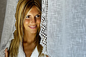 Young woman in a bath robe behind curtais, smiling, Hotel, South Tyrol, Italy