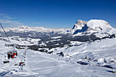 Menschen auf einem Sessellift über verschneiter Skipiste, Seiser Alm, Dolomiten, Südtirol, Italien, Europa