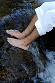 Die Beine eines Mannes auf einem Stein in einem Bach, Südtirol, Italien, Europa