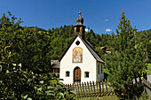 Kapelle mit Wandmalerei zwischen Bäumen im Sonnenlicht, Villnöss, Eisacktal, Südtirol, Italien, Europa