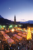 Christmas market at Walther square in the evening, Bolzano cathedral in the background, Bolzano, South Tyrol, Italy