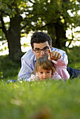 Father and daughter (2-3 years) lying in meadow, English Garden, Munich, Bavaria, Germany