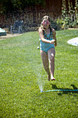 Young girl runs through yard sprinkler