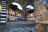 Rila monastery at dusk, arcades and outer wall of Mary`s Birth Church with frescos, lighted arcades of the residential building, Bulgaria