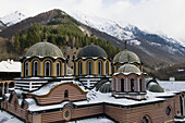 Rila monastery, cupolas of Mary`s Birth Church, snow-covered Rila mountains and surrounding forests, Bulgaria