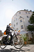 Zwei Geschäftsleute auf Fahrrädern auf Kopfsteinpflaster, München, Bayern, Deutschland