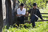 Two older men sitting on bench in village, Maramures, Romania