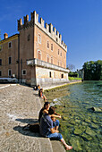Menschen sitzen am Ufer vor der Skaligerburg, Lazise, Gardasee, Venetien, Italien, Europa