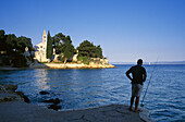 Angler on the beach in front of Dominican abbey under blue sky, Brac island, Croatian Adriatic Sea, Dalmatia, Croatia, Europe