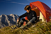 Young woman sitting in front of a tent in the mountains, Tyrol, Austria, Europe