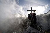 Wanderer an einem Gipfelkreuz zwischen Wolken, Wettersteingebirge, Bayern, Deutschland, Europa