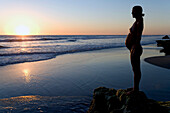 Schwangere Frau steht auf Felsen am Strand, Sonnenuntergang, Strand bei Conejo, Baja California Süd, Mexiko