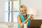 Adult, Adults, At home, Blonde, Blondes, Caucasian, Caucasians, Color, Colour, Computer, Computers, Contemporary, Cup, Cups, Daytime, eyeglasses, Facing camera, Fair-haired, Female, glasses, grin, grinning, Hobbies, Hobby, Home, human, indoor, indoors, in