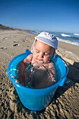 5 Monate altes Baby badet in einem Eimer mit Wasser am Strand, Nine Palms, Baja California Süd, Mexiko