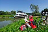 Frau sitzt in einer Wiese an der Donau und liest, Ardagger Markt, Niederösterreich, Österreich