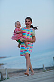 Girl carrying baby on jetty, Formentera, Balearic Islands, Spain