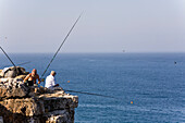Fishermen sitting on a rock fishing, near Cape Cabo de Sao Vicente, Atlantic Ocean, Sagres, Algarve, Portugal
