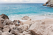 Mädchen sitzt lesend auf einem Fels in einer Bucht, Golfo di Orosei, Sardinien, Italien, Europa