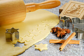 Stars cutted out of cookies dough, cookie cutters for Christmas cookies, rolling pin, wood pattern, cinnamon and star anise laying at worktop