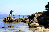 Menschen auf Felsen am Strand von Baia Sardinia, Costa Smeralda, Nord Sardinien, Italien, Europa