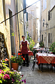Kellnerin und Tische eines Restaurants in einer Gasse, Castelsardo, Nord Sardinien, Italien, Europa