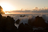 Wellen brechen an Felsen aus Lavastein bei Sonnenuntergang, Porto Moniz, Madeira, Portugal