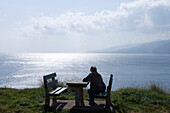 Frau sitzt am Picknicktisch und genießt Meerblick nahe Ponta de Sao Laurenco, nahe Canical, Madeira, Portugal