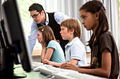 Male teacher helping pupils in computer room, Hamburg, Germany