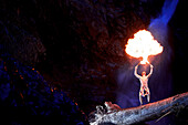 Young man standing on trunk in front of a waterfall while breathing fire, See, Tyrol, Austria