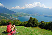 Woman sitting on meadow and looking over Lake Como, Monti Lariani, Lombardy, Italy