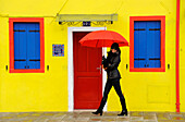 Woman with umbrella walking along the street, Burano, Venice, Veneto, Italy