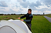Man pitching a tent, Waldhusen, Pellworm island, Schleswig-Holstein, Germany