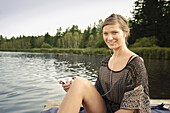 Junge Frau sitzt auf einem Steg am Starnberger See, hört Musik, Bayern, Deutschland